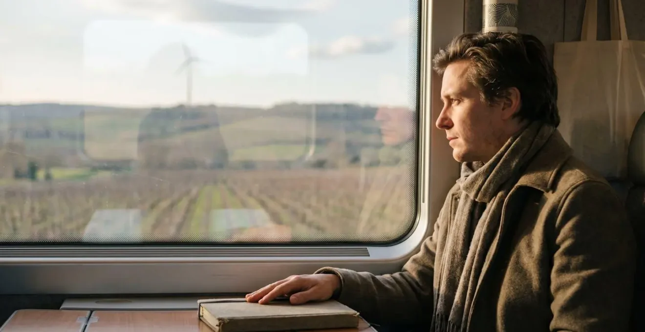 Voyageur contemplant un paysage ferroviaire français depuis une fenêtre de train
